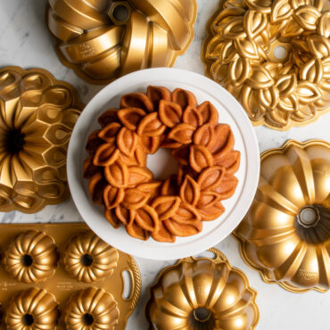 Plain Laurel Wreath Bundt on white cake stand surrounded by various gold Bundt Pans