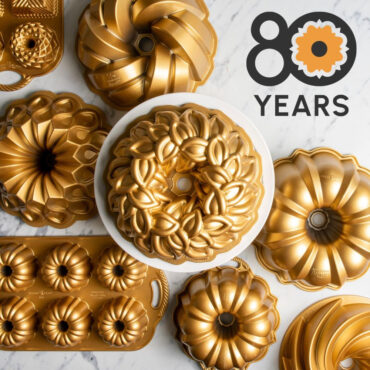 Laurel Wreath Bundt on white cake stand surrounded by various gold Bundt Pans and Nordic Ware 80th Anniversary Logo- 80 Years text