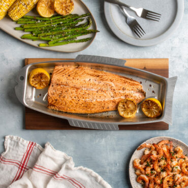 naturals fish and seafood griller with salmon on cutting board  with plated corncobs, asparagus, and shrimp