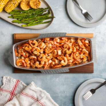 naturals fish and seafood griller with shrimp on cutting board  with plated corncobs, asparagus
