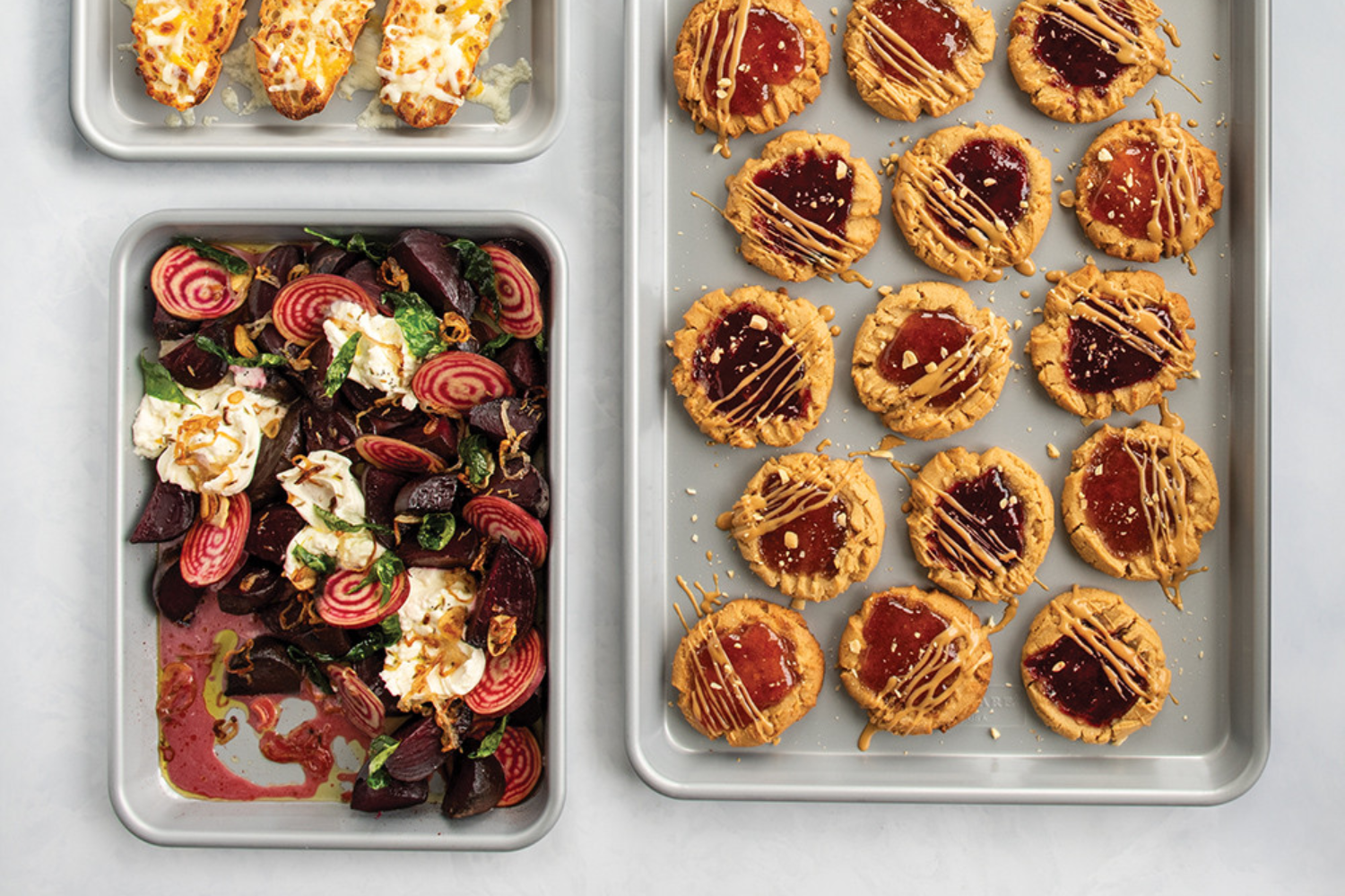 3-Piece Brilliant Bakeware Nonstick Sheet Pan Set with cookies, veggies, and cheesy bread baked on them. 