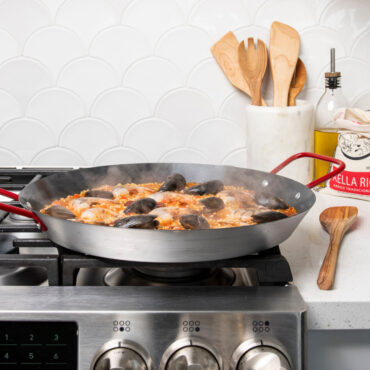 paella pan with saffron rice, shrimp, mussels, and vegetables arranged on stovetop