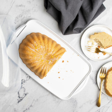 overhead image of lemon fluted loaf cake cut in half in keeper on marble countertop with small plates with cake slices