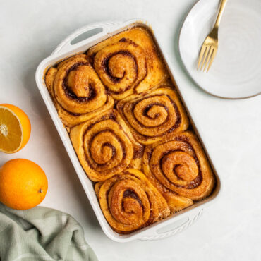 overhead view of cardamom rectangular baking pan with cinnamon buns, oranges and plate nearby