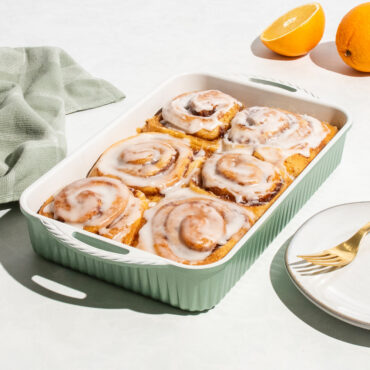 cardamom rectangular baking pan with glazed cinnamon buns, oranges and plate nearby