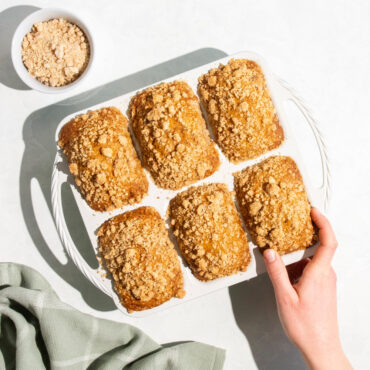 overhead view of aluminum mini loaf pan with 8 rectangular cavities filled with cakes, hand on one cake
