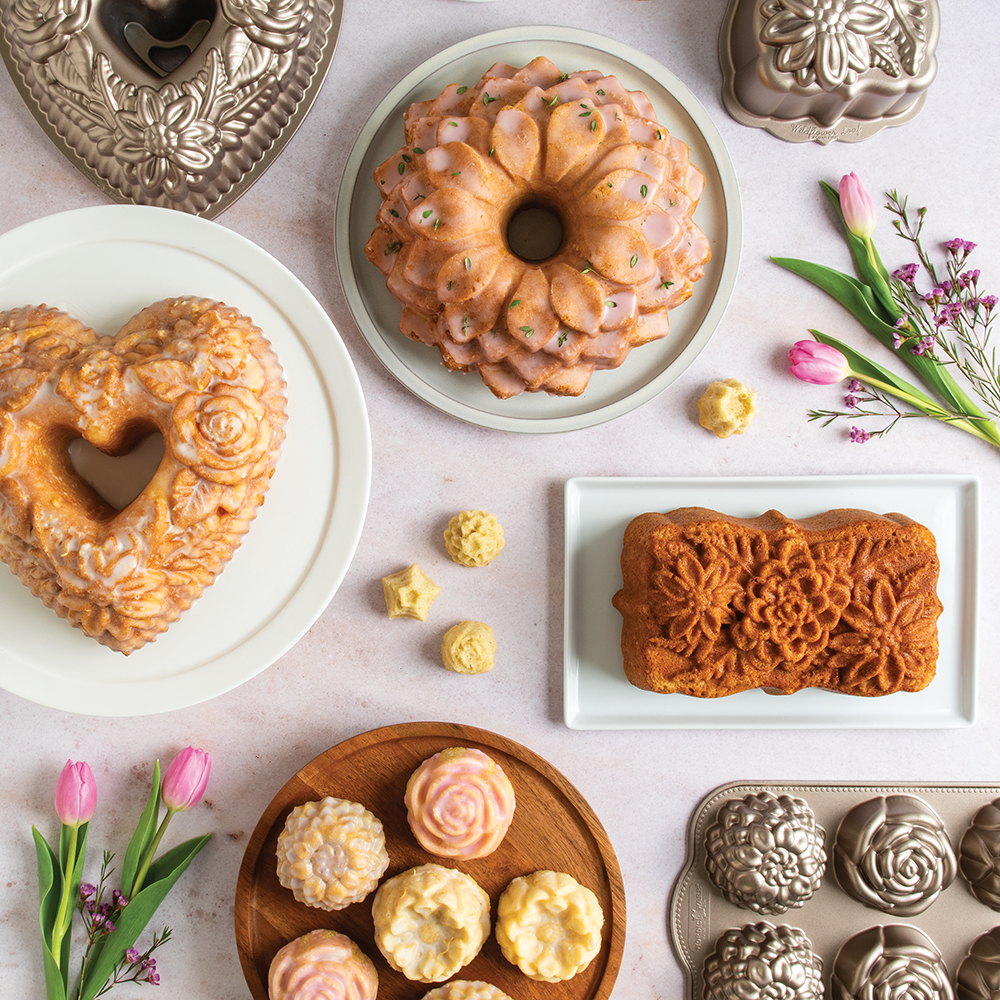 Group image of floral Bundt cakes, loaf cakes, and mini flower cakes with floral bakeware pan on a pink table.
