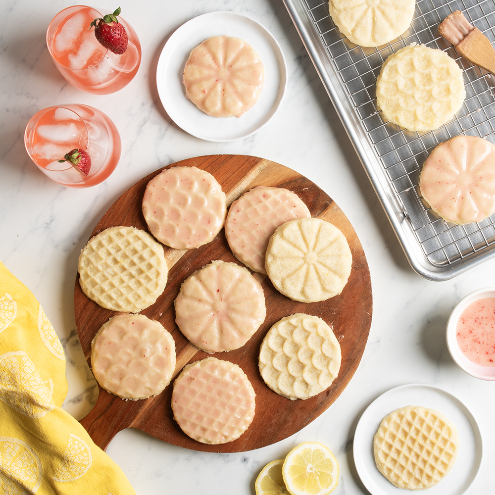 Image of a baked lemon stamped shortbread cookies in Heirloom cookie stamp designs glazed with a strawberry pink glaze in styled scene