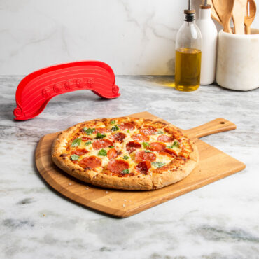 lifestyle scene of freshly cut supreme topping pizza on cutting board placed on marble countertop with rock the boat pizza cutter in background
