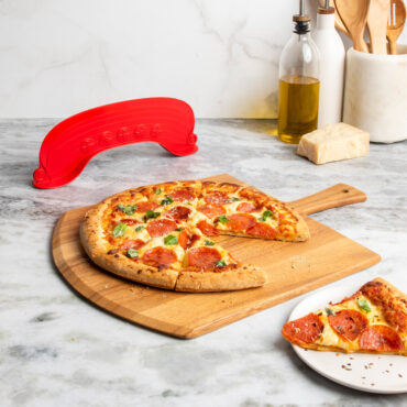 lifestyle scene of freshly cut supreme topping pizza on cutting board placed on marble countertop with rock the boat pizza cutter in background
