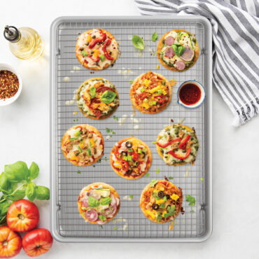 overhead of various meat and veggie flat breads on cooling rack nested inside brilliant big sheet pan