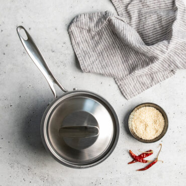overhead of basalt 1.5qt saucepan with lid placed on countertop and dish of seasoning next to it