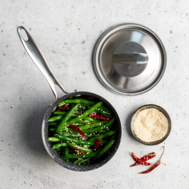 overhead of basalt 1.5qt saucepan filled with string beans placed on countertop with lid and dish of seasoning next to it