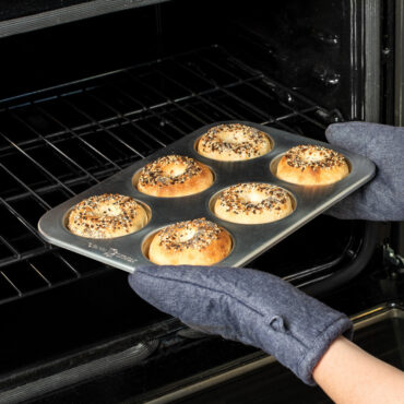 hands wearing oven mitts taking freshly baked bagels on pan out of oven
