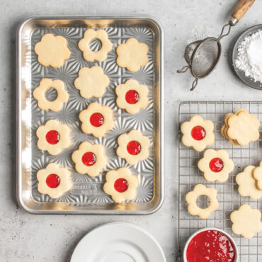 overhead of novelty shape cookies on starburst quarter sheet pan; cooling grid with jam nearby