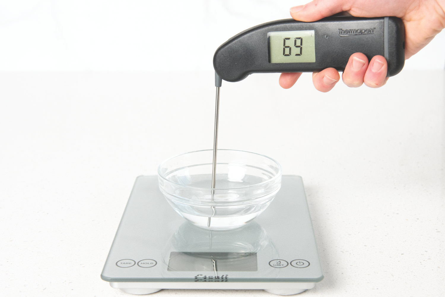 Hand with thermometer taking the temperature of the water used to feed sourdough starter showing 69 degrees.