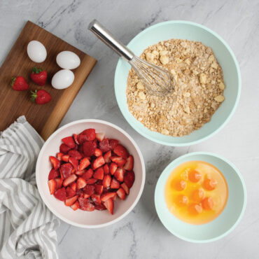 Nordic Ware 3 piece seaglass and white 5 quart, 3.5 quart and 2 quart bowls filled with dough, egg yolks, and strawberries