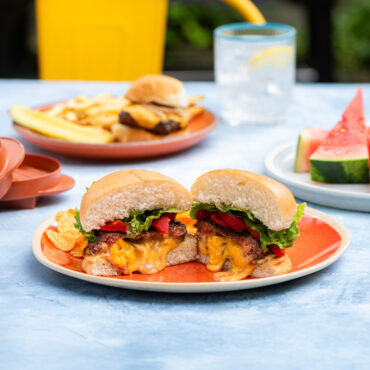 outdoor table scene with plated burger cut in half with melted cheese inside patty