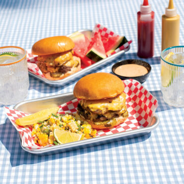 double cheese burgers and veggies on set of two burger serving trays staged on outdoor table scene