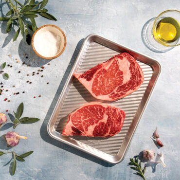 overhead of raw steaks placed on prep grill and serve tray