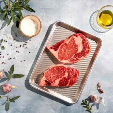 Raw ribeye steak on Nordic Ware aluminum 3-in-1 prep tray with raised grill ridges, natural silver finish