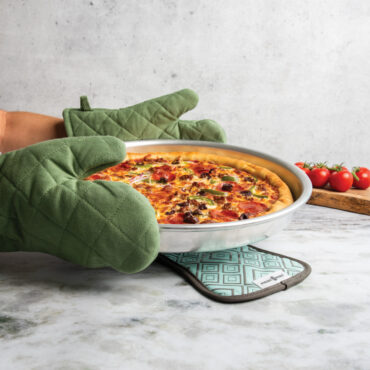 hands with oven mitts holding deep dish pizza pan with supreme style pizza above hot pad