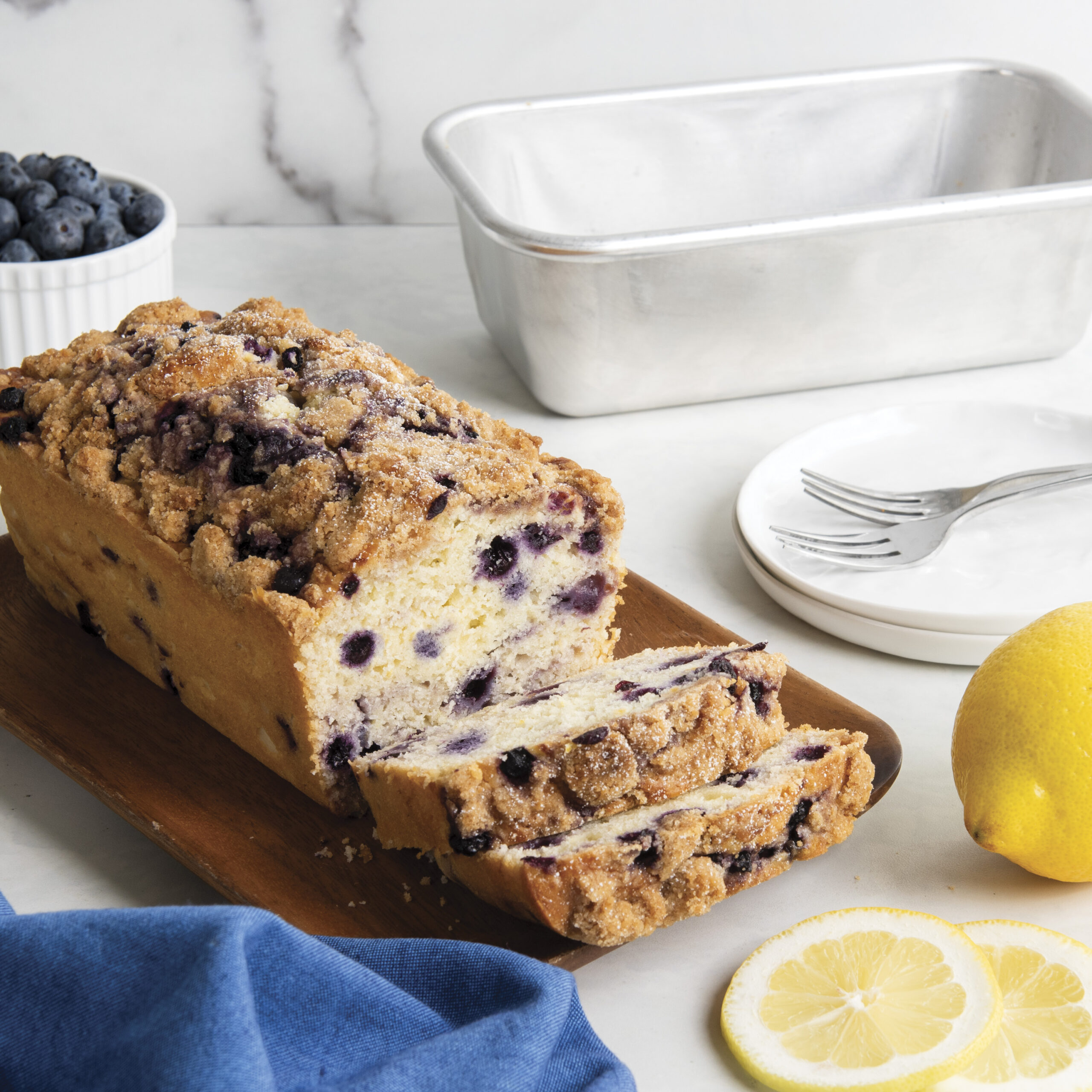 Image of lemon blueberry breakfast bread sliced on the counter with loaf pan in background.