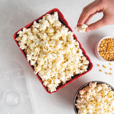 hand grabbing popcorn from Nordic Ware Movie Night Popcorn Popper with translucent lid