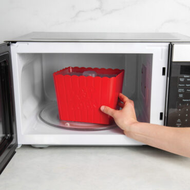 hand placing Nordic Ware Movie Night Popcorn Popper with translucent lid into microwave