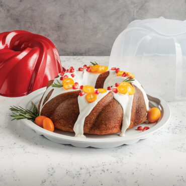 Red Nordic Ware aluminum bundt pan with clear plastic cake keeper dome, frosted bundt cake inside